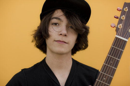 Portrait of boy with guitar standing against yellow background