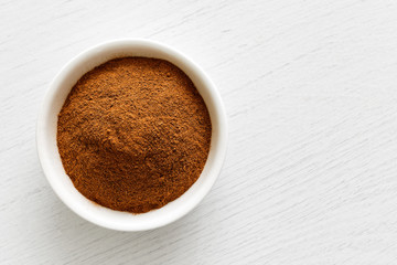 Finely ground cinnamon in white ceramic bowl isolated on white wood background from above. © Moving Moment