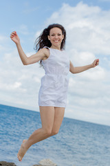 Girl in white jumping against sea looking at camera smiling