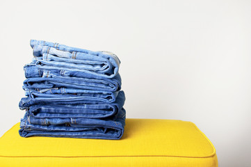 Jeans blue denim fabric clothing textiles on a bright yellow pouf on a white wall background. The concept of clothing, fashion, style.