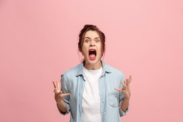 The young emotional angry woman screaming on pink studio background