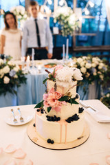 White wedding cake with peonies, groom and bride on background
