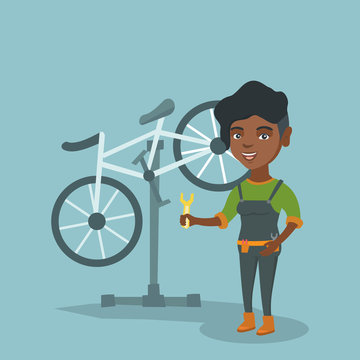 Young african-american bicycle mechanic showing a spanner on the background of broken bicycle