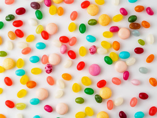 Many scattered colorful sweets, candies, lollipops on  white background, top view. Jelly beans.