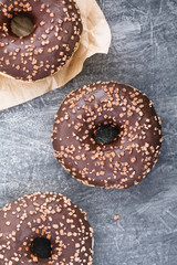 Three chocolate donuts on a grey textured background. Flat lay.