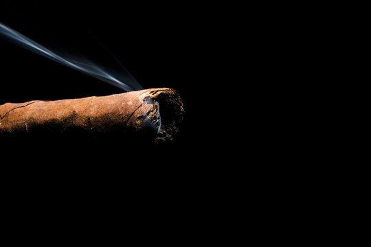 Cigar burnt with smoke on the tip on a black background