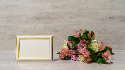 Colorful bouquet of roses, chrysanthemum and alstroemeria flowers with empty photoframe on wooden background