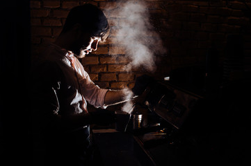 Close-up image of barista man using coffee-making machine to steam milk in cafe.