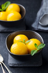 Mango ice cream, tropical fruit sorbet in black bowl on stone background.