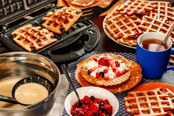 Waffles with whipped cream, berries and tea. Waffles are fried from dough in a waffle maker.