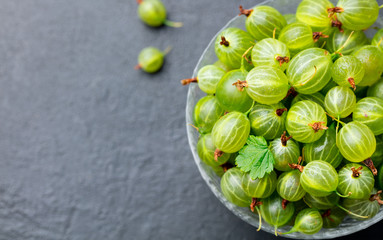 Gooseberries in glass bowl on black stone slate background. Top view. Copy space.
