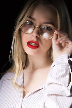Portrait of glamor blonde woman in glasses wearing blouse with naked shoulders, posing with dramatic studio light