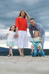 Fototapeta premium Woman and man with girls on tricycle on cloudy sky