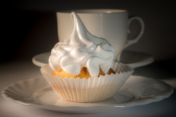 Cupcake with white icing on a plate and a cup of tea. Sweet dessert with white glaze close-up.