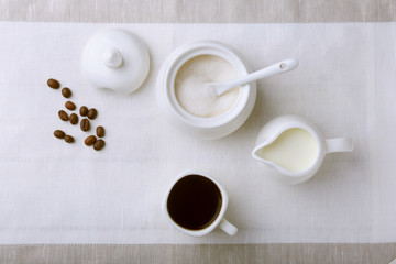 Cup of hot coffee espresso, coffee beans, jug of milk, and bowl with sugar on white background for copy space. Coffee concept.