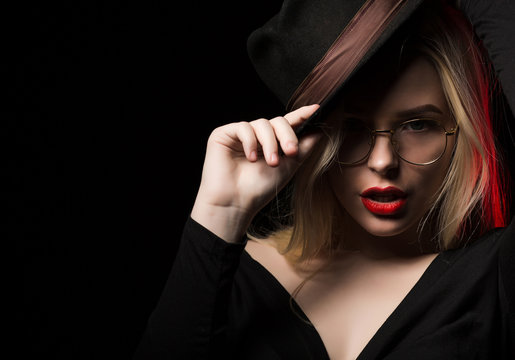 Seductive young woman wearing brown hat and glasses, posing at black background