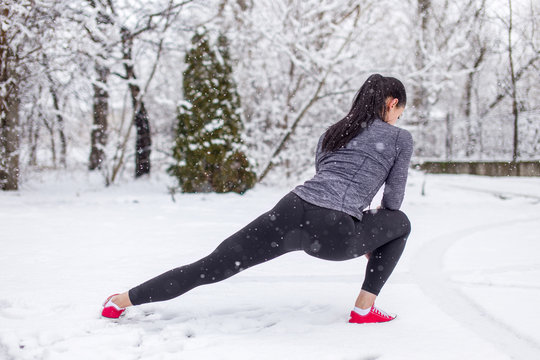 Fit woman doing stretching exercise in snow outdoors