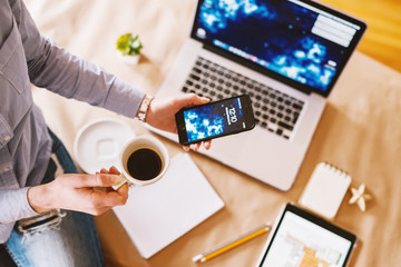 Successful businesswoman checking the time on mobile while sitting on the desk and having a coffee break in the office.