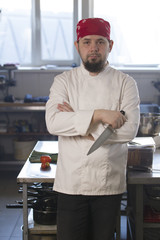 Portrait of a fashionable chef in bandana holding a knife in a kitchen