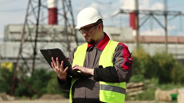 Power engineering specialist with personal computer at heat electric power station. Worker in hard hat at heat electric power station, engineering supervision. Factory worker with tablet pc