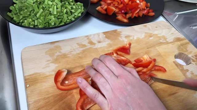 Time lapse of Caucasian female hands cutting in slices red pepper uncooked on a wooden cutting board in a kitchen with a knife.