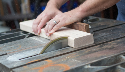 A close up photo of a man sawing through a piece of wood on a table saw with sawdust flying.