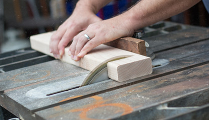 A close up photo of a man sawing through a piece of wood on a table saw with sawdust flying.