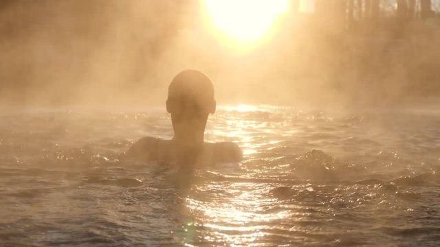 Geothermal spa. Woman relaxing in hot spring pool outdoors. Girl enjoying bathing in a blue water lagoon tourist attraction at sunset. Slow motion