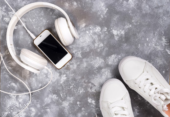 Flat lay Of White Sneakers On stone Background with phone and headphones.