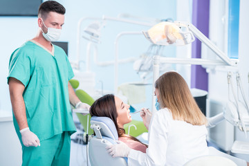 Obraz premium people, medicine, stomatology and health care concept - happy female dentist with mirror checking patient girl teeth up at dental clinic office while male assistant is waiting behind.