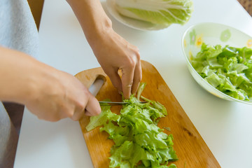 A woman is cutting leaves of a salad on a wooden board.