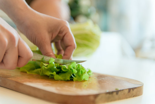 A woman is cutting leaves of a salad on a wooden board.
