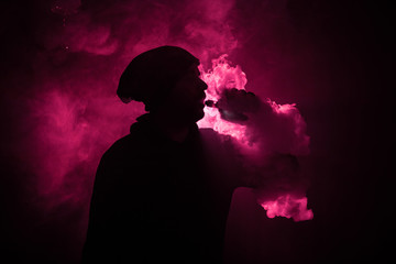 Vaping man holding a mod. A cloud of vapor. Black background. Vaping an electronic cigarette with a...