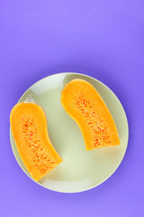 Halves of a pumpkin on a green plate, pumpkin on an ultraviolet background, vegetables pop art, minimalism, orange vegetables on a purple background, art, pumpkin for a designer, vegan