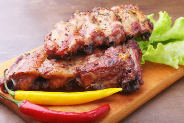 grilled barbecued ribs with lettuce leaves, hot chili pepper and sauce on wooden cutting board.