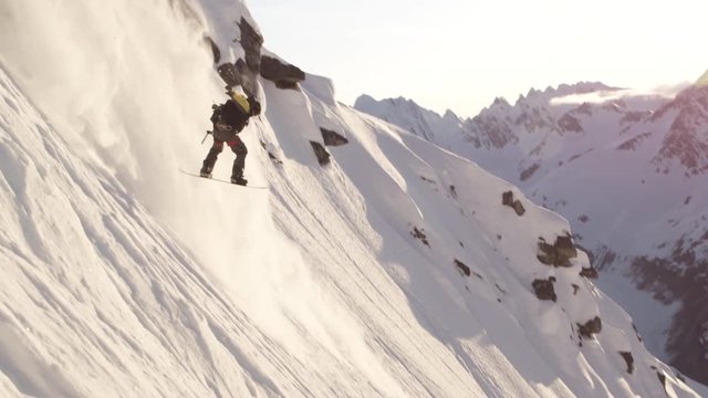 Snowboarders does jump off side of mountain, slow motion