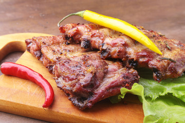 grilled barbecued ribs with lettuce leaves, hot chili pepper and sauce on wooden cutting board.