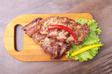grilled barbecued ribs with lettuce leaves, hot chili pepper and sauce on wooden cutting board.