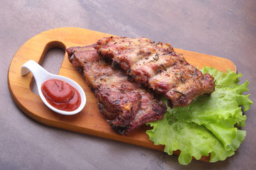 grilled barbecued ribs with lettuce leaves, hot chili pepper and sauce on wooden cutting board.