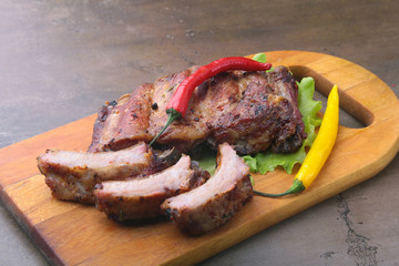 grilled barbecued ribs with lettuce leaves, hot chili pepper and sauce on wooden cutting board.