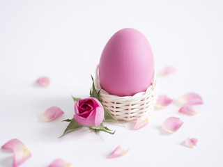 Easter greeting card with Easter egg and petals of pink roses on white background with copy space.