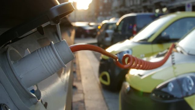 Close up of an yellow electric vehicle's plugged in charge port. Zoom out.