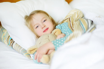 Adorable little girl sleeping in the bed with her toy. Tired child taking a nap under white blanket.