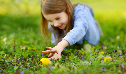 Adorable little girl hunting for Easter egg in blooming spring garden on Easter day