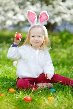 Adorable little girl hunting for easter egg in blooming spring garden on Easter day