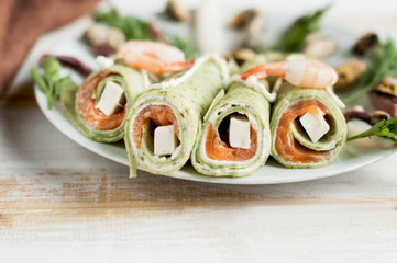 Green pancakes close-up with salmon stuffing and cheese on white wooden background.