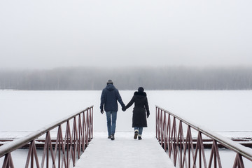 Couple is walking together hand in hand on pier. 