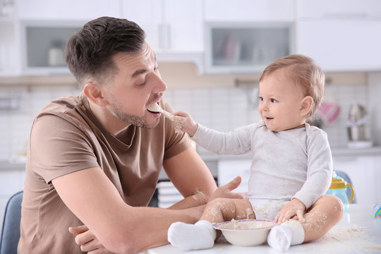 Cute baby boy feeding his father in kitchen