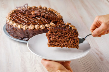 Chocolate cake Prague with chocolate buttercreamy frosting. A woman's hand holds a slice of cake over a plate. Homemade baking. Closeup view.