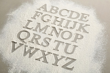 Silhouettes of alphabet letters on scattered flour